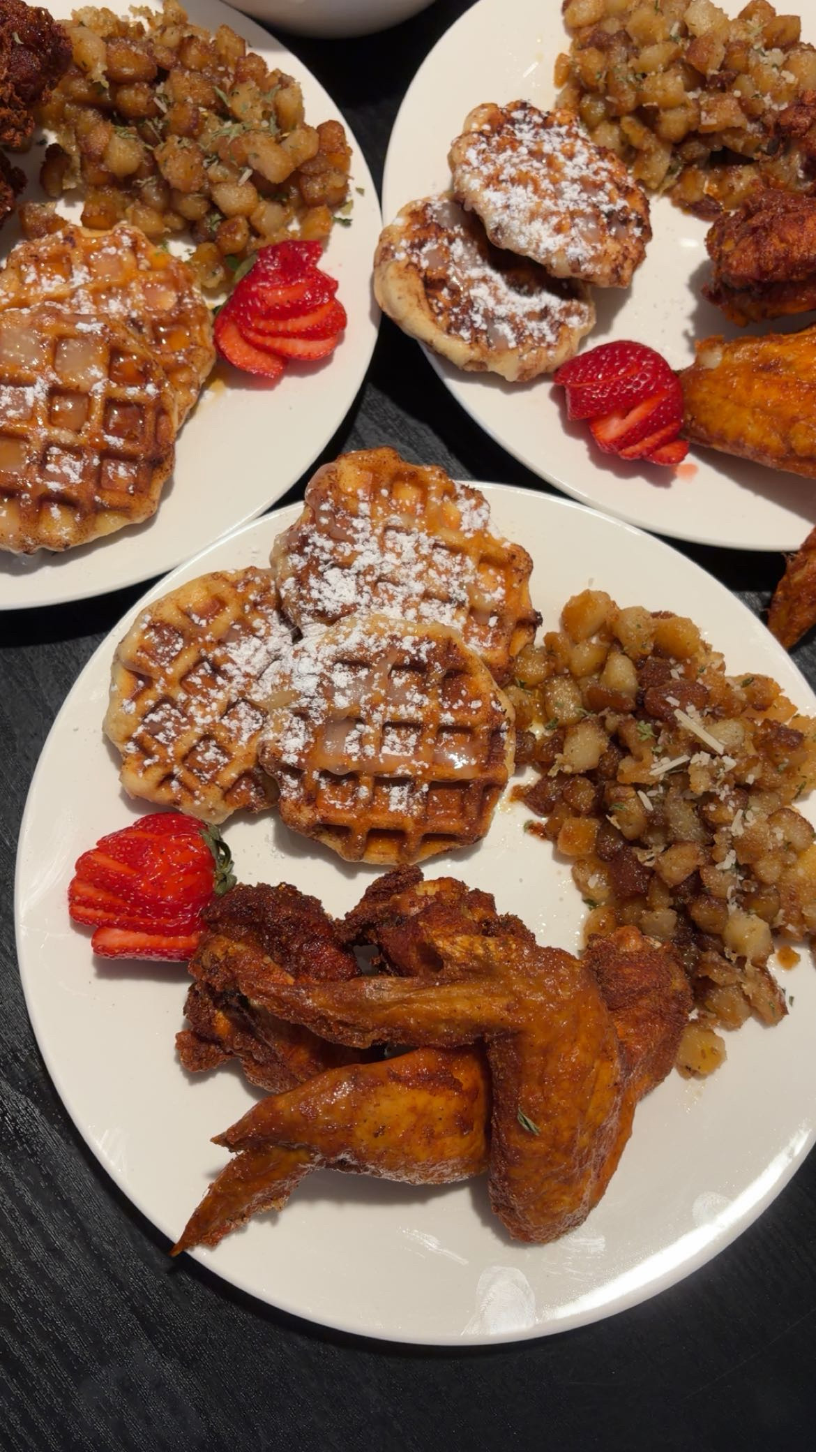 Chicken and waffles with seasoned breakfast potatoes and strawberries on white plates