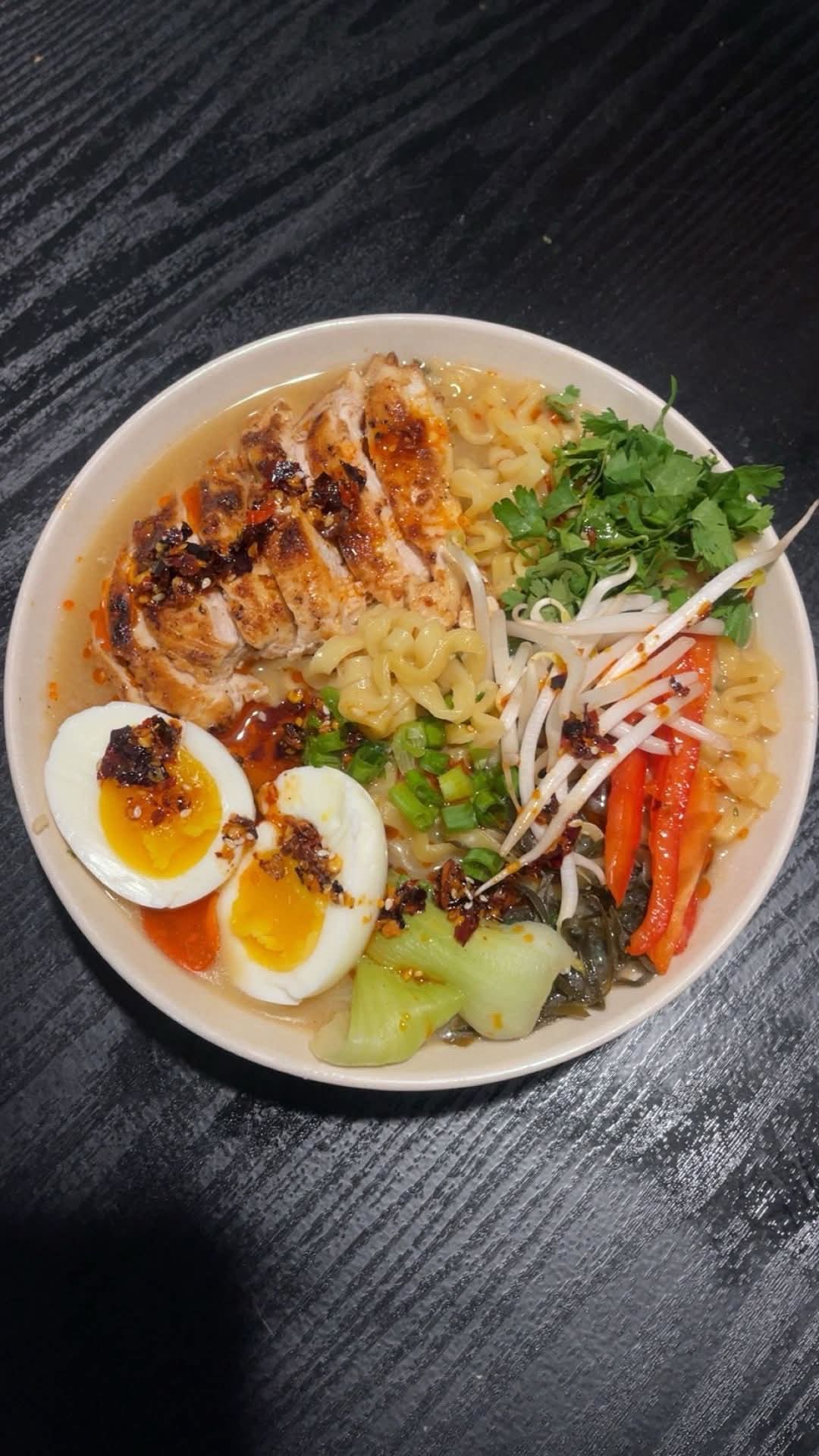 Chef-prepared ramen bowl with chicken, egg, vegetables, and herbs